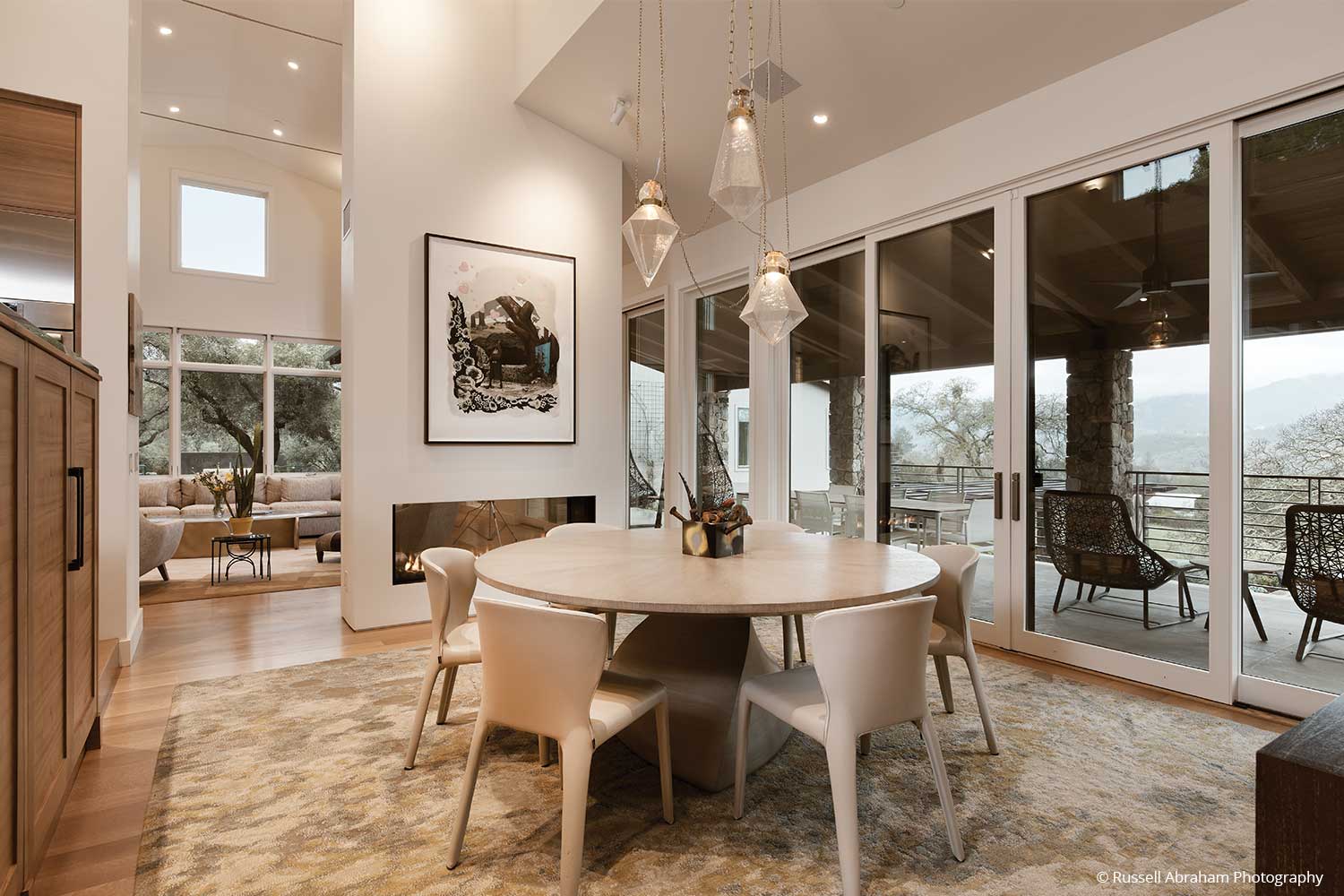 A tall dining space captures vast outdoor views through a wall of glass sliding doors and various large windows.