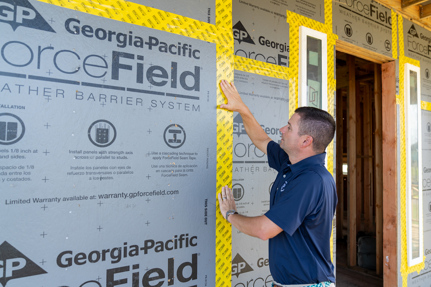 Landon Wright from Prestige Custom Builders wears a blue polo and presses ForceField® Premium Tape installed on a home.