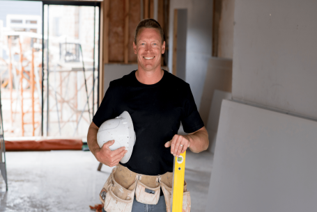 Smiling trade contractor holding hardhat and level on custom-home jobsite